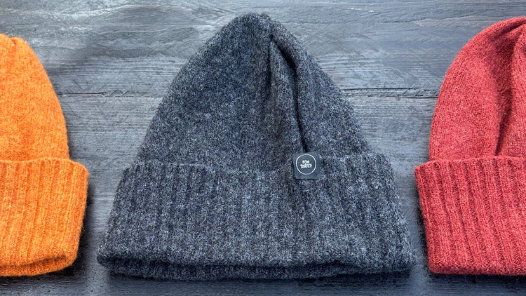 Charcoal wool beanie with doubled brim, flanked by rust orange and sienna brown beanies on dark wood