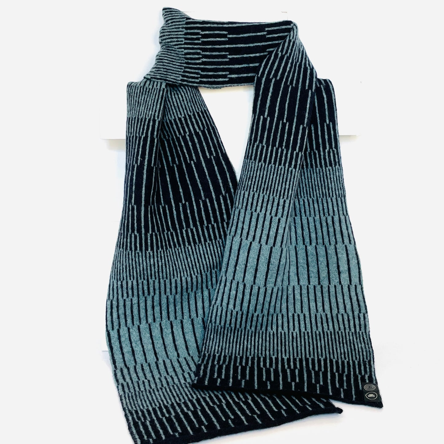 Blue Caspian and Navy Blue handcrafted merino Lambswool striped Reverb Scarf hanging on a white display stand  against a neutral background. Pom Shanty Knitwear.