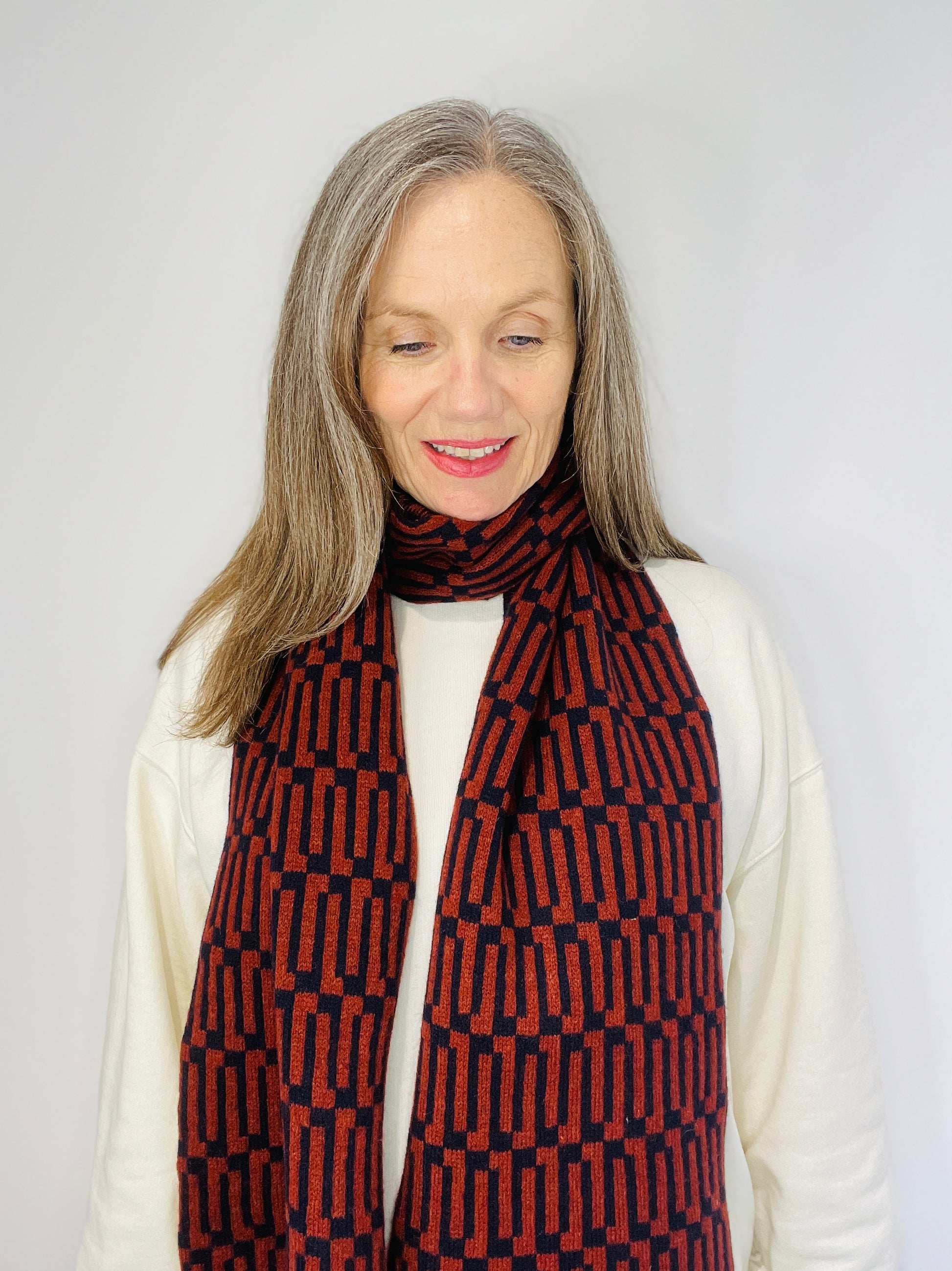 Beautiful sexy woman in a white top wearing a Brown Sienna and Navy handcrafted merino Lambswool Geometric patterned Scarf on a neutral background Pom Shanty Knitwear