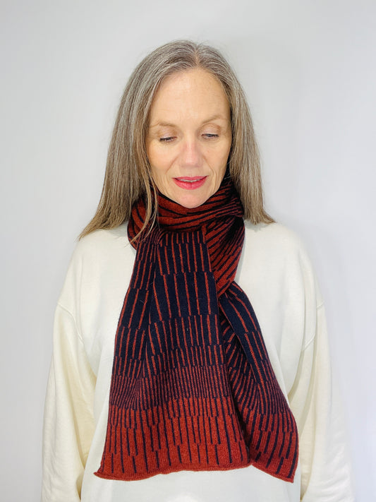 beautiful sexy woman in a white top wearing Brown Sienna and Navy Blue handcrafted merino Lambswool striped Reverb Scarf against a neutral background. Pom Shanty Knitwear