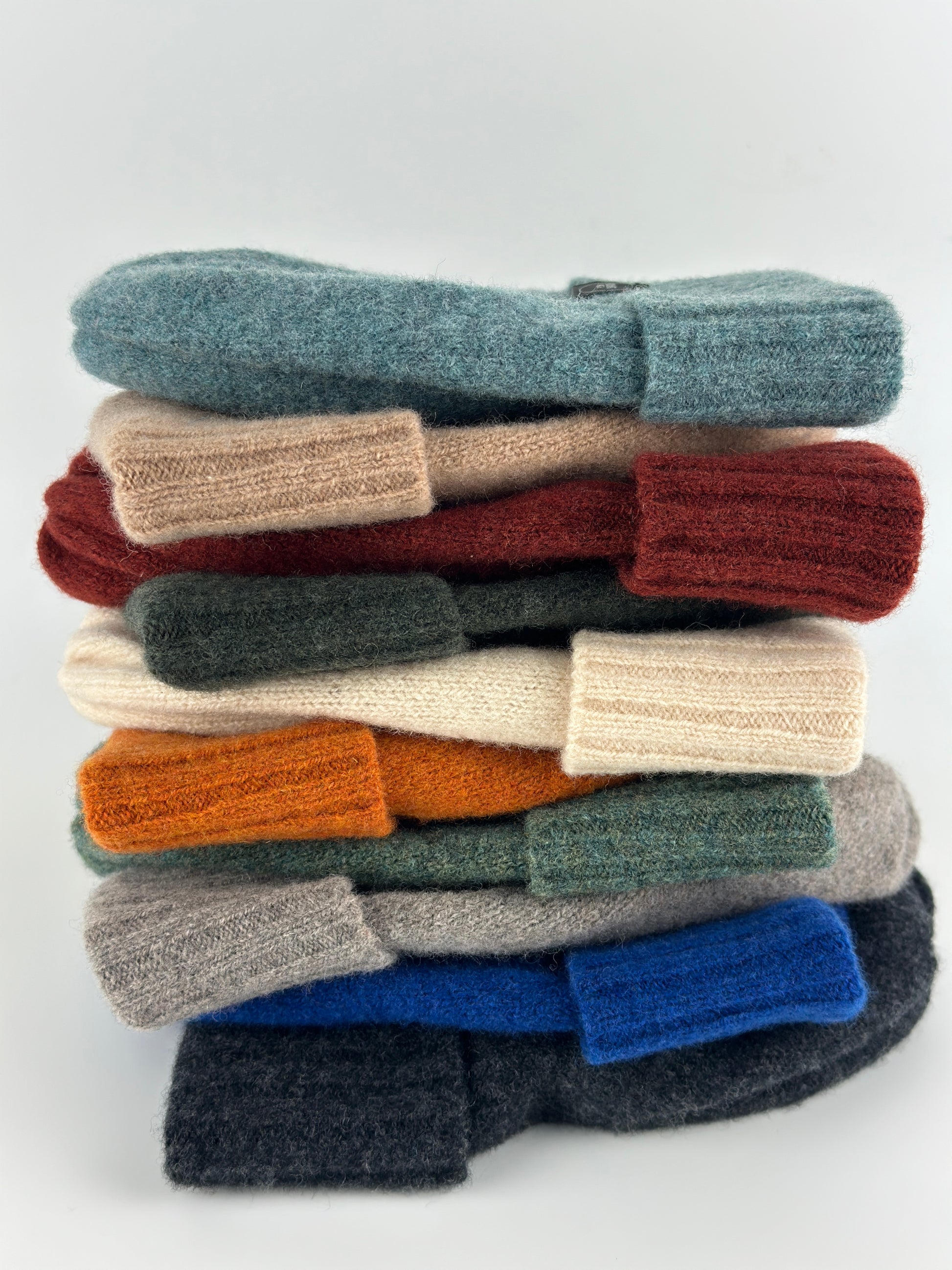 stack of multicoloured merino lambswool knitted beanies with double ribbed brims on a white background