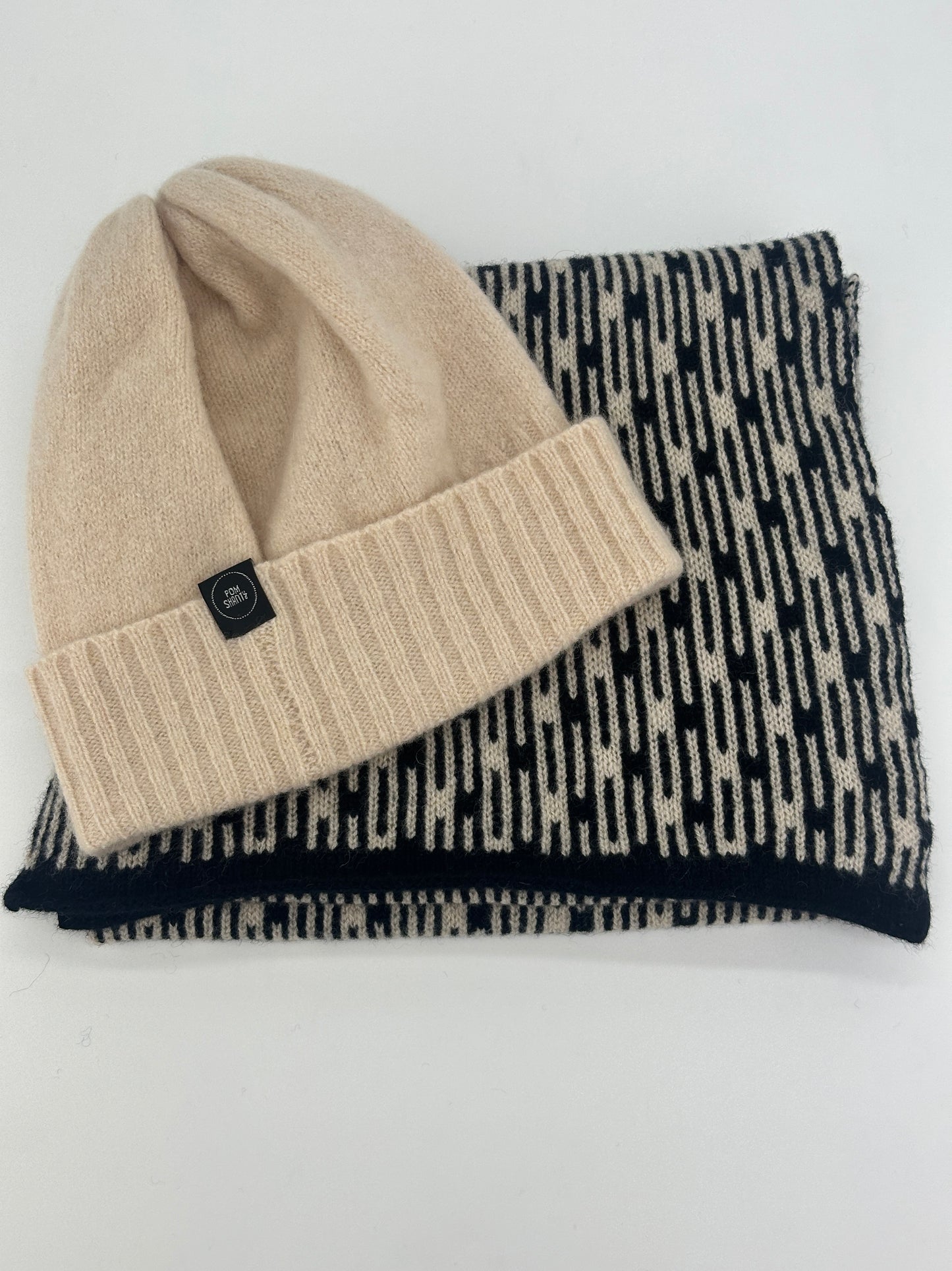 Black and Oatmeal Metropolis geometric patterned handcrafted merino lambswool scarf folded on a white table with an oatmeal handcrafted merino lambswool beanie on top.Pom Shanty Knitwear.
