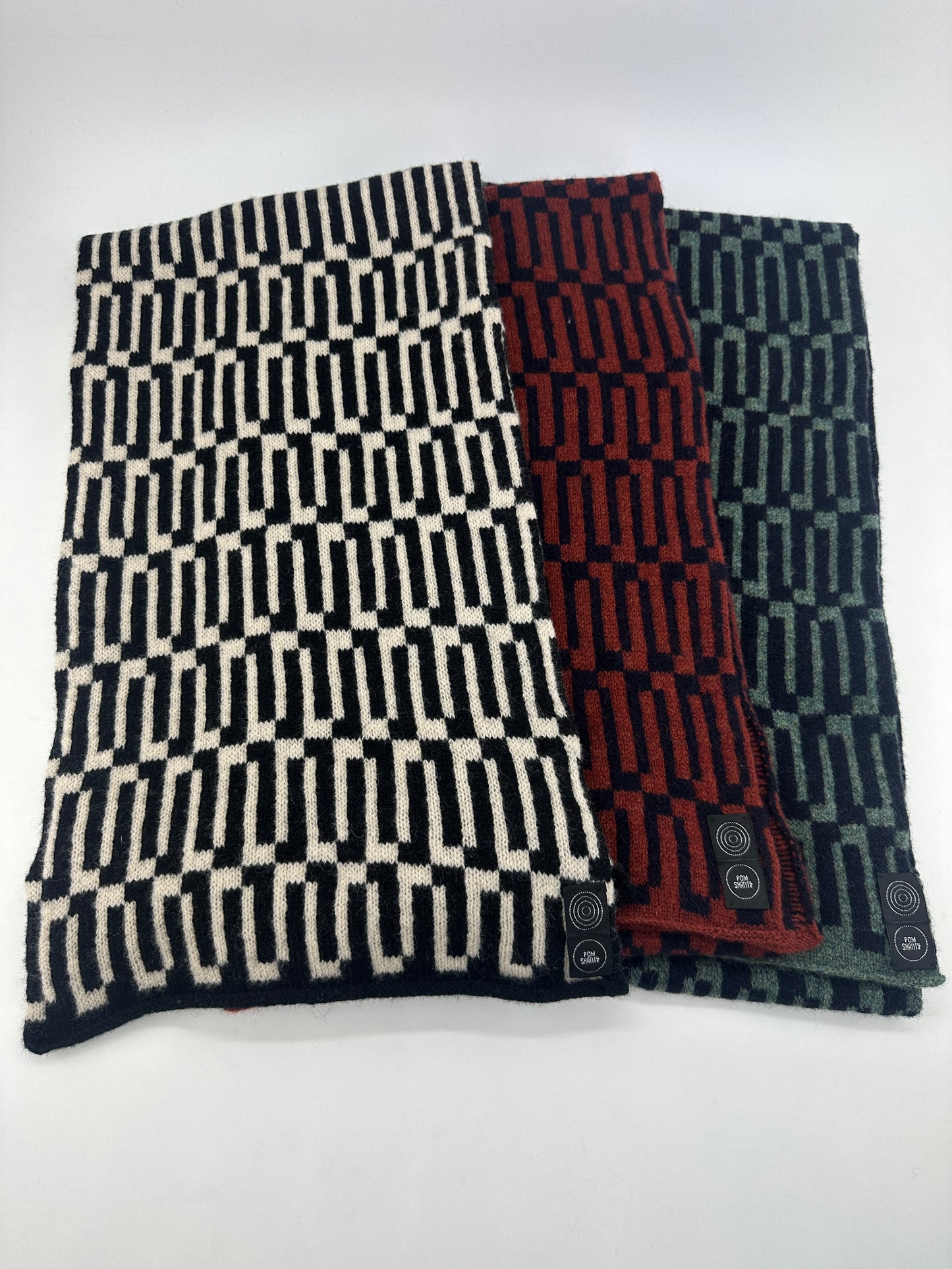 Three different coloured geometric patterned merino lambswool handcrafted scarves spread out on a white table.