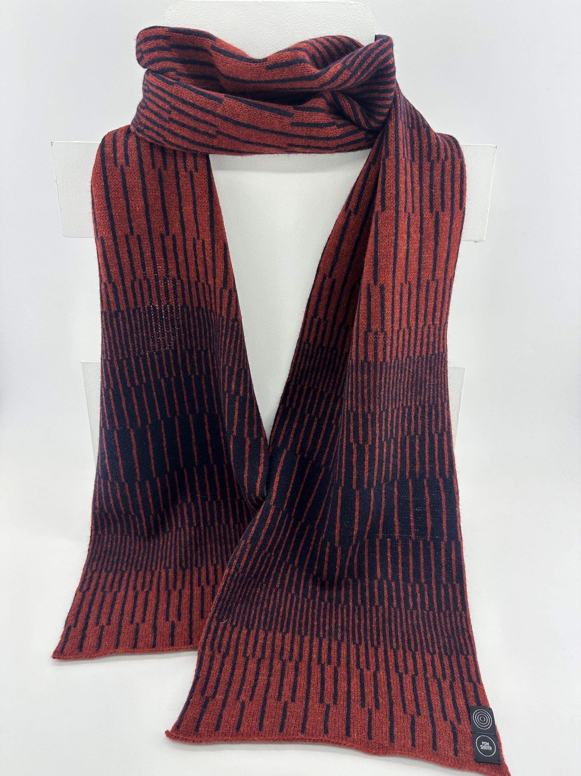 Sienna Brown and Navy Blue handcrafted merino Lambswool striped Reverb Scarf hanging on a white display stand  against a neutral background. Pom Shanty Knitwear.