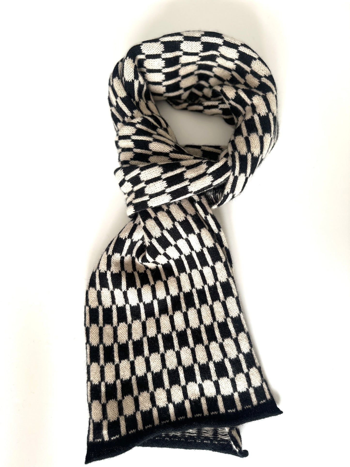 Black and oatmeal handcrafted Merino Lambswool geometric patterned Morse scarf curled up on a white table. Pom Shanty Knitwear.