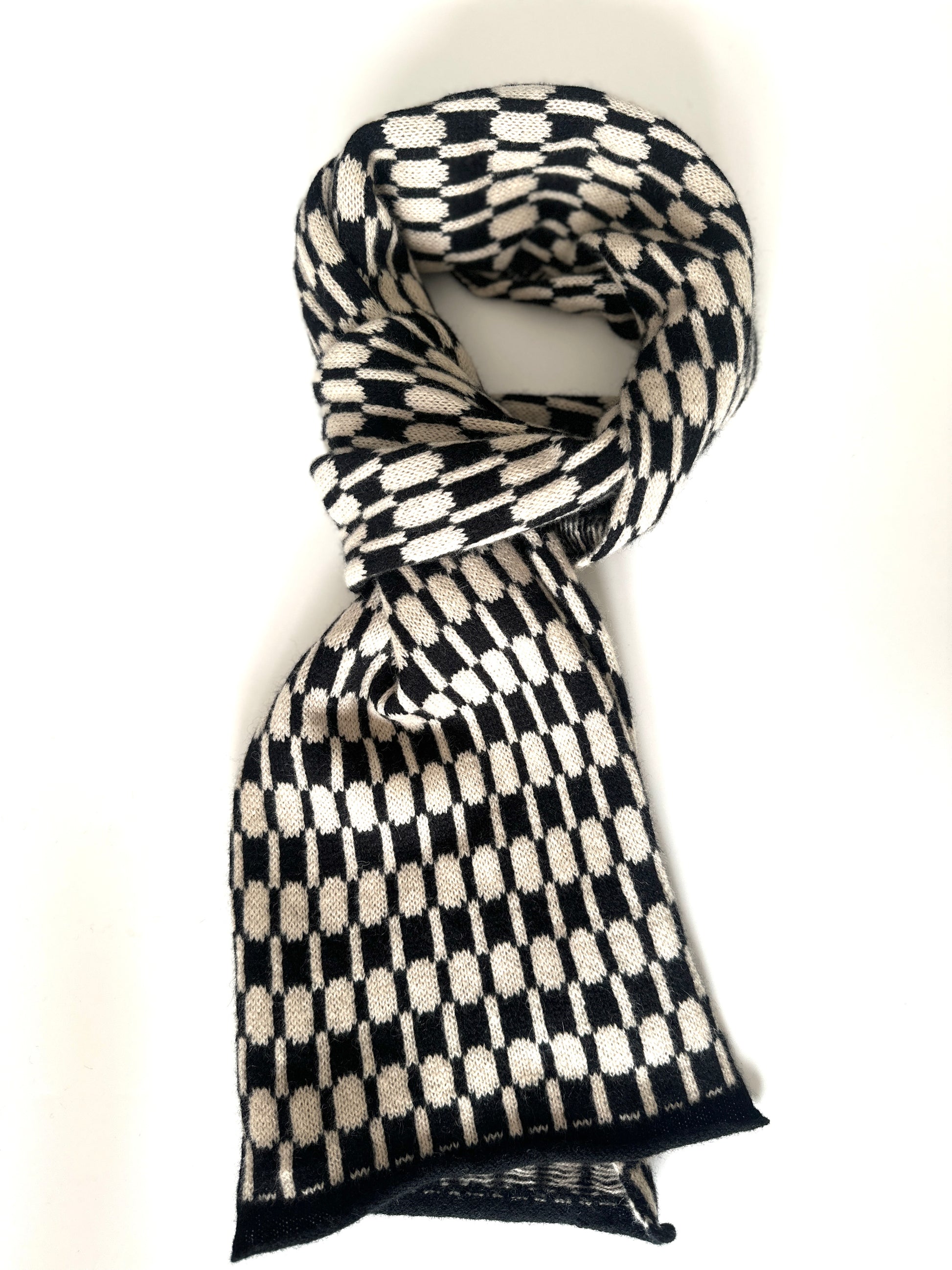 Black and oatmeal handcrafted Merino Lambswool geometric patterned Morse scarf curled up on a white table.  Pom Shanty Knitwear.