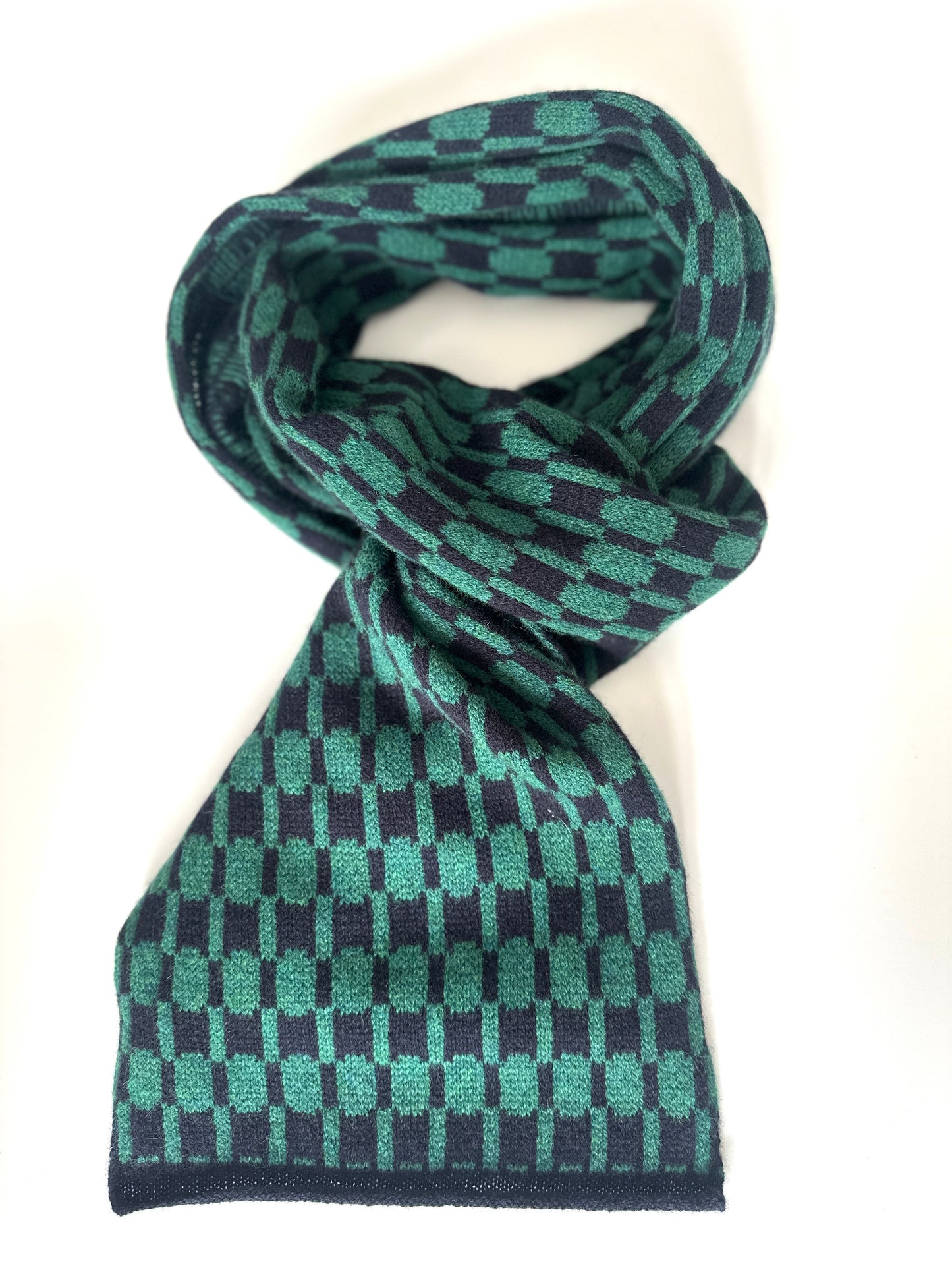Navy blue and cossack green handcrafted Merino Lambswool geometric patterned Morse scarf curled up on a white table.  Pom Shanty Knitwear.