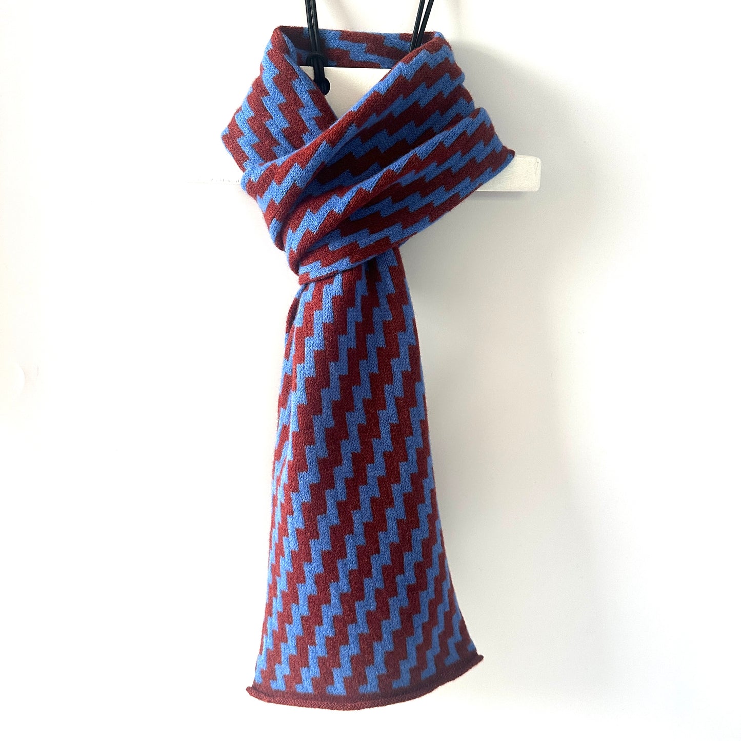 rick rack geometric patterned sienna brown and cornflower blue merino lambswool scarf hanging on a white hanger against a white background. Pom Shanty Knitwear.