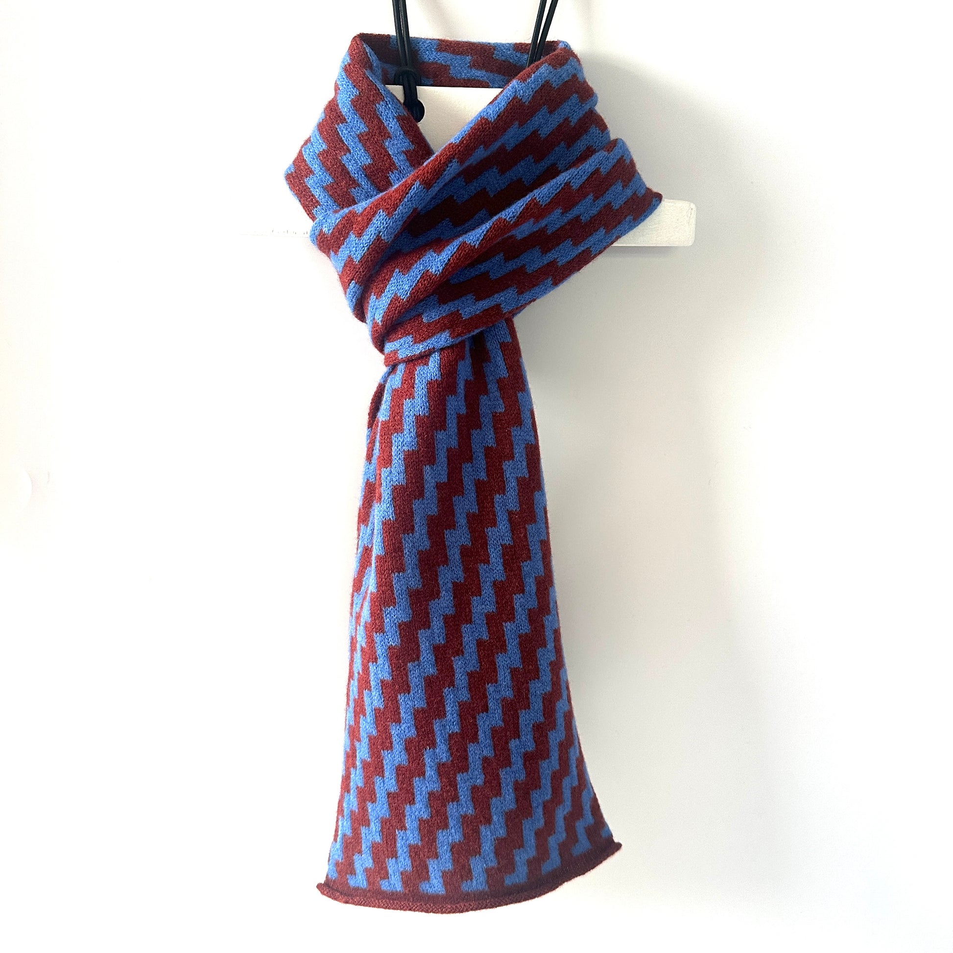 rick rack geometric patterned sienna brown and  cornflower blue merino lambswool scarf hanging on a white hanger against a white background. Pom Shanty Knitwear.