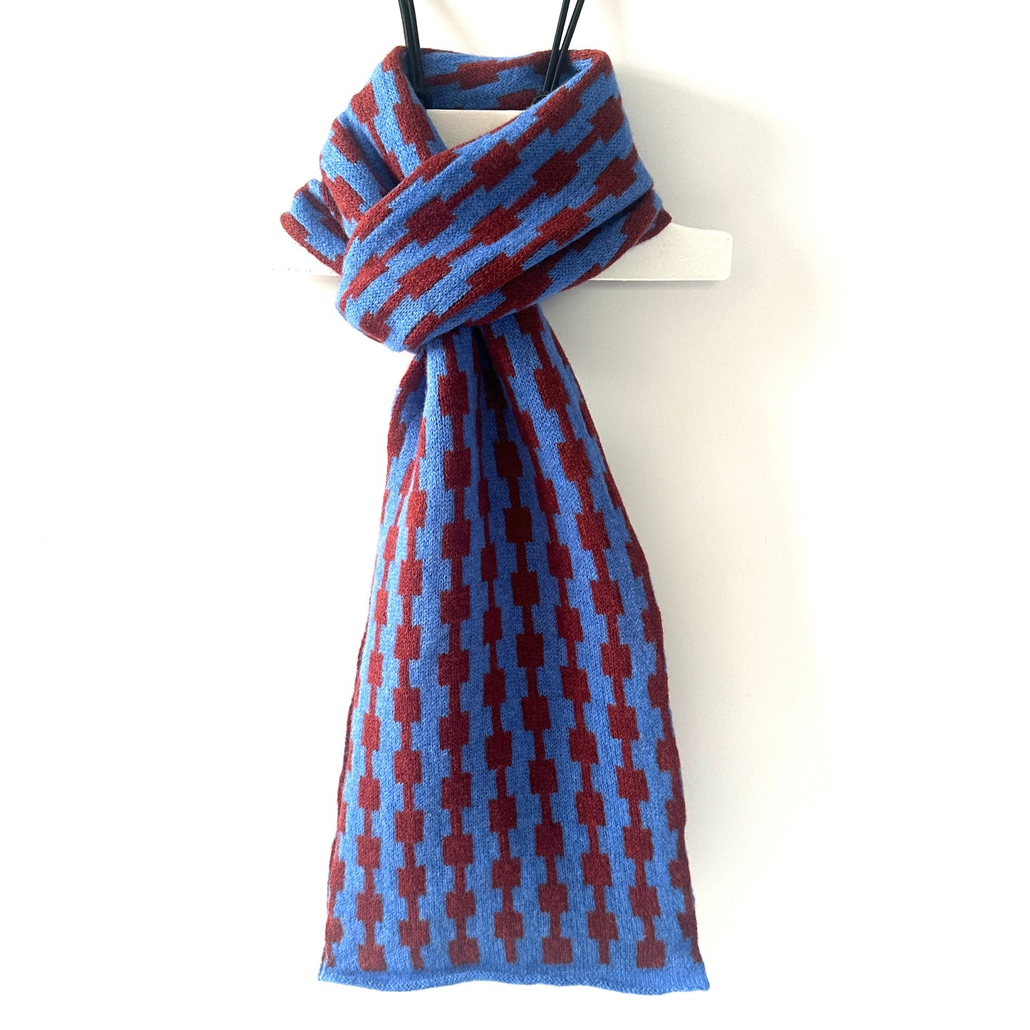 Cornflower blue and sienna brown handcrafted Merino Lambswool geometric patterned Pulse scarf on a white hanger against a white background. Pom Shanty Knitwear.