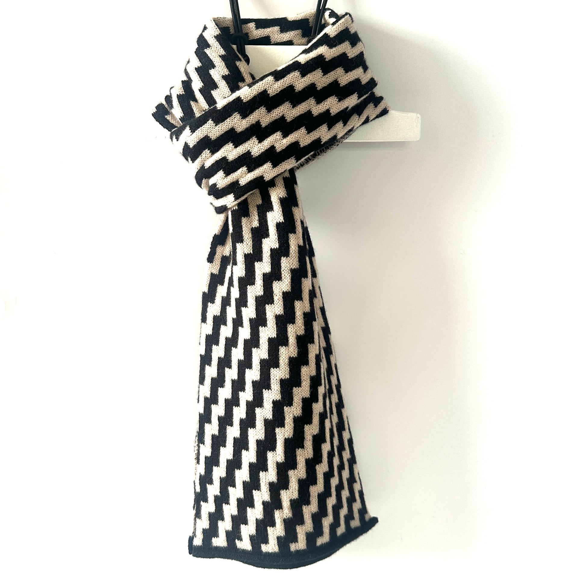 rick rack geometric patterned black and oatmeal merino lambswool scarf tied on a white against a white background. Pom Shanty Knitwear.