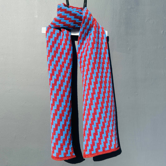 rick rack geometric patterned sienna brown and  cornflower blue merino lambswool scarf draped on a white hanger against a grey background. Pom Shanty Knitwear.