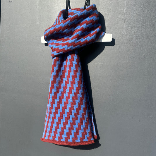 rick rack geometric patterned sienna brown and  cornflower blue merino lambswool scarf hanging on a white hanger against a grey background. Pom Shanty Knitwear.