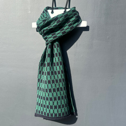 Navy blue and cossack green handcrafted Merino Lambswool geometric patterned Morse scarf on a white hanger against a grey background.  Pom Shanty Knitwear.