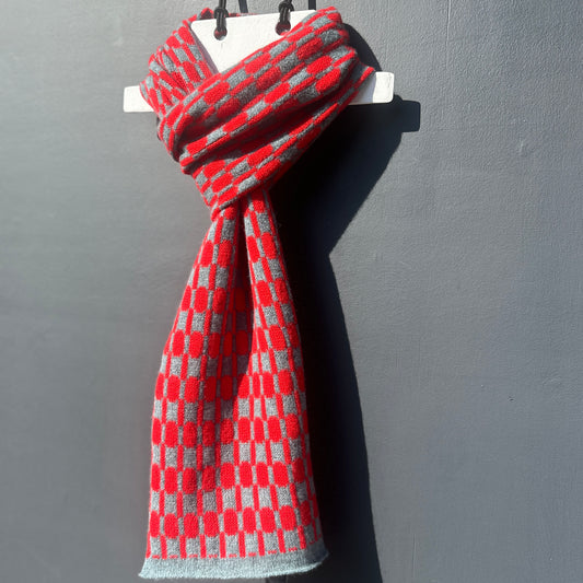 Red and Caspian Blue handcrafted Merino Lambswool geometric patterned Morse scarf on a white hanger against a grey background.  Pom Shanty Knitwear.