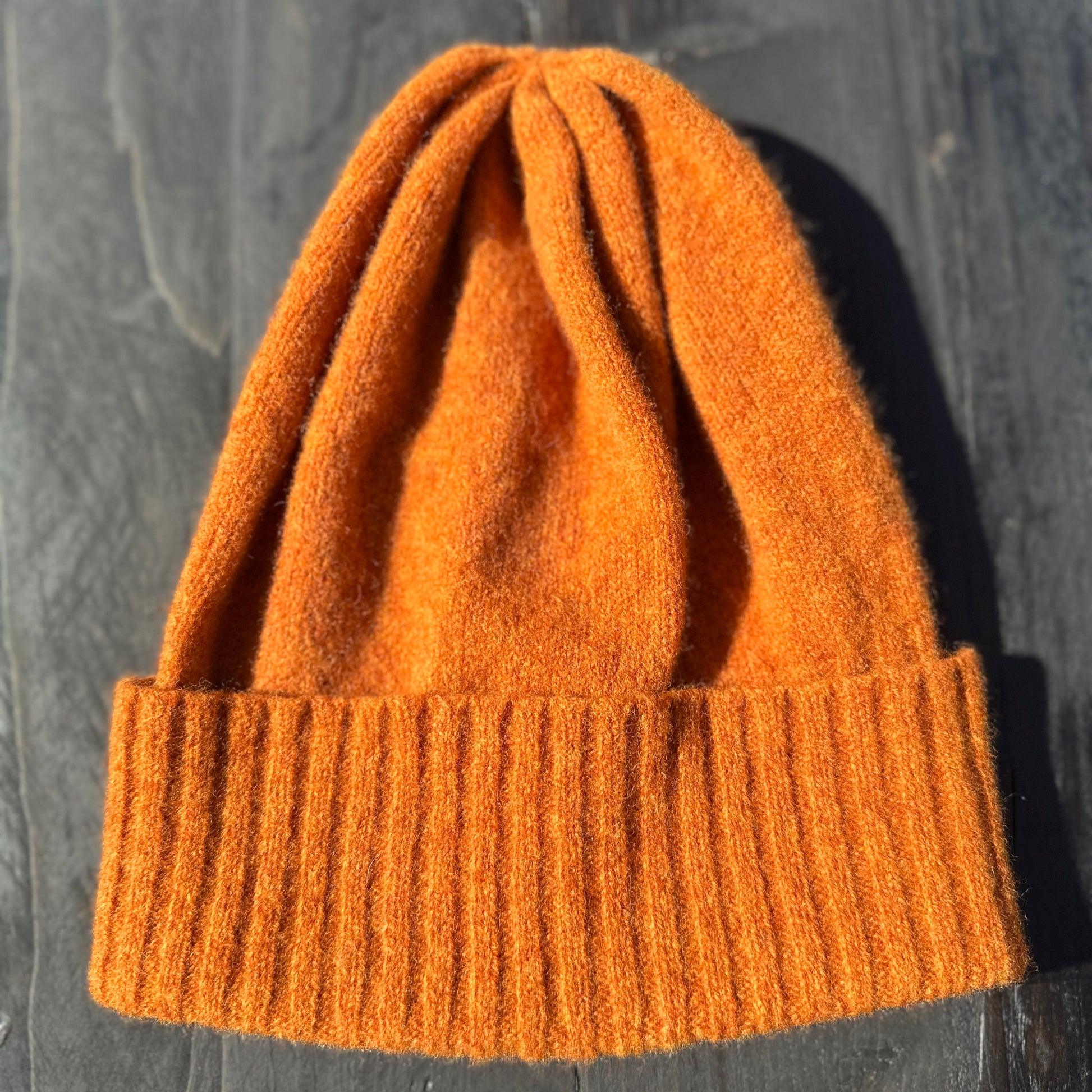 Rust coloured merino lambswool handcrafted knitted beanie with a double ribbed brim lying flat on a grey table