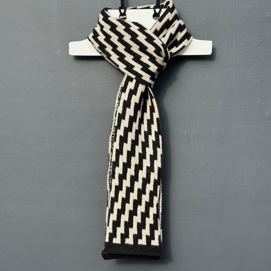 rick rack geometric patterned black and oatmeal merino lambswool skinny scarf tied on a hanger on a rod against a grey background. Pom Shanty Knitwear.