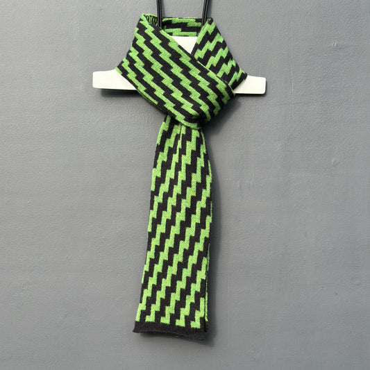 rick rack geometric patterned watercress green and black merino lambswool skinny scarf hanging on a rod against a grey background. Pom Shanty Knitwear.