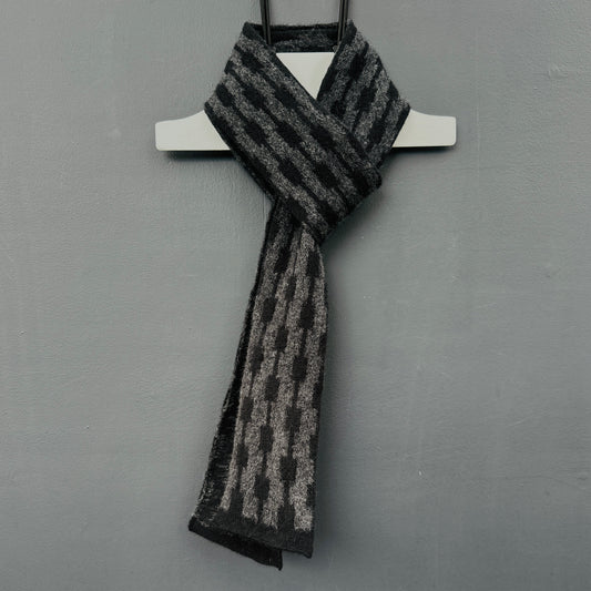 geometric patterned charcoal grey and black merino lambswool skinny scarve hanging on a rod against a grey background