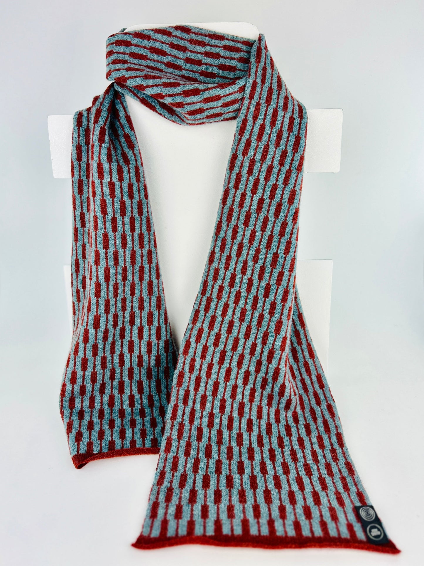sienna brown and caspian blue merino lambswool geometric patterned scarf on a rack on a plain background.