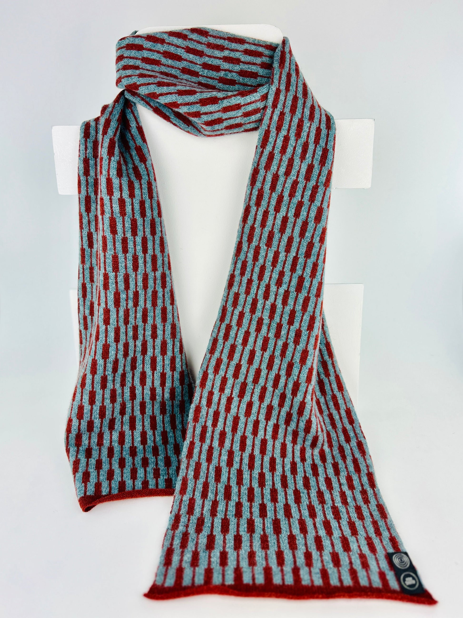 sienna brown and caspian blue merino lambswool geometric patterned scarf on a rack on a plain background.