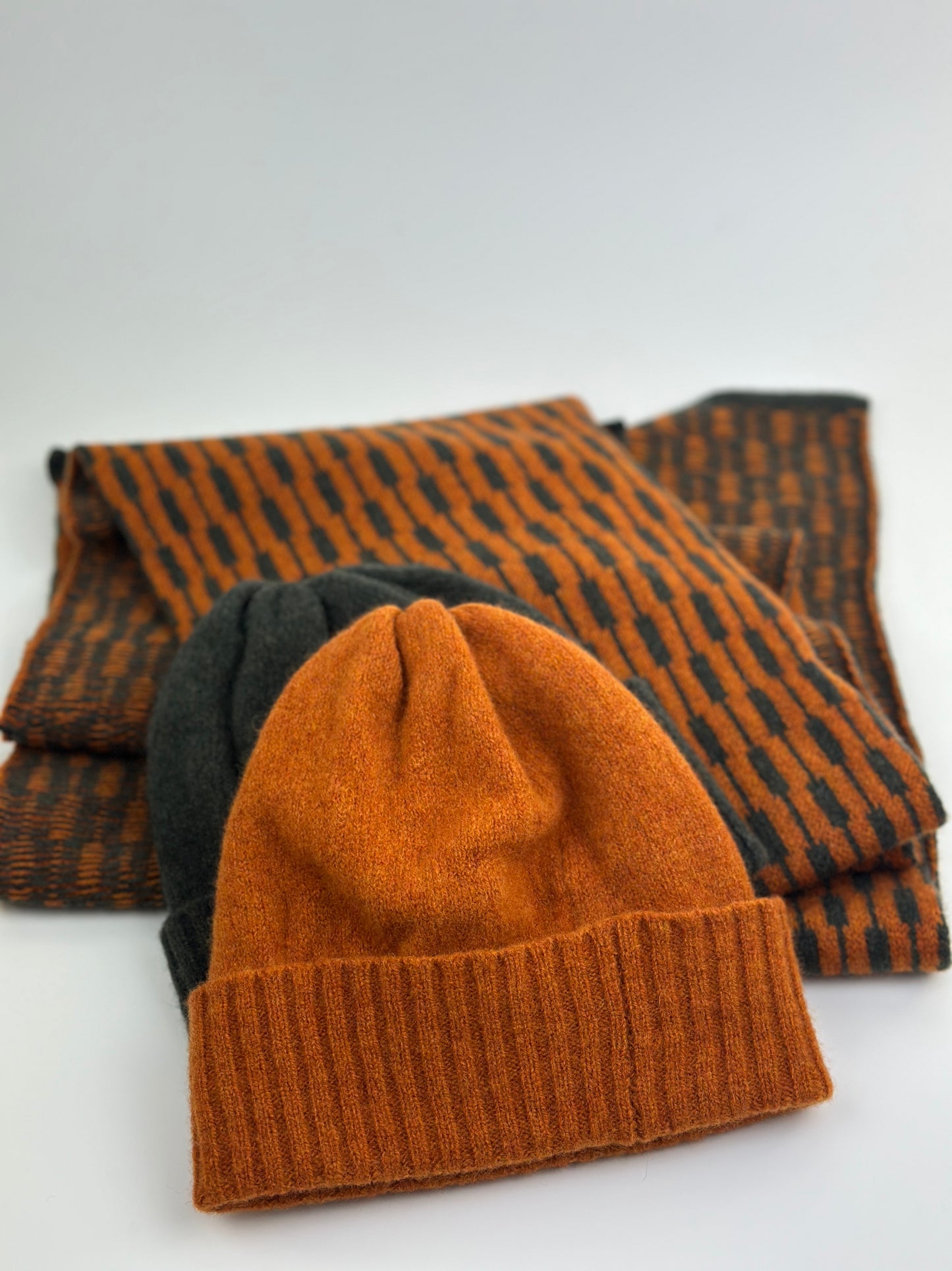 Rust coloured merino lambswool handcrafted knitted beanie shown with a grey beanie and a rust and grey scarf