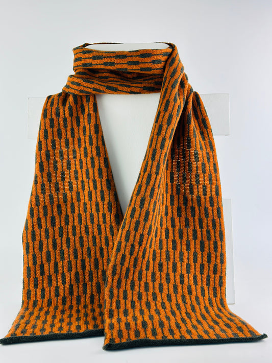 rust and olive green merino lambswool geometric patterned scarf on a rack on a plain background.