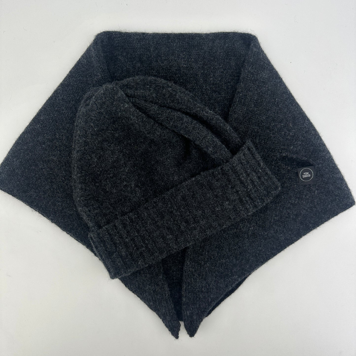 Charcoal grey coloured merino lambswool handcrafted knitted beanie with a double ribbed brim and kerchief lying flat on a white background