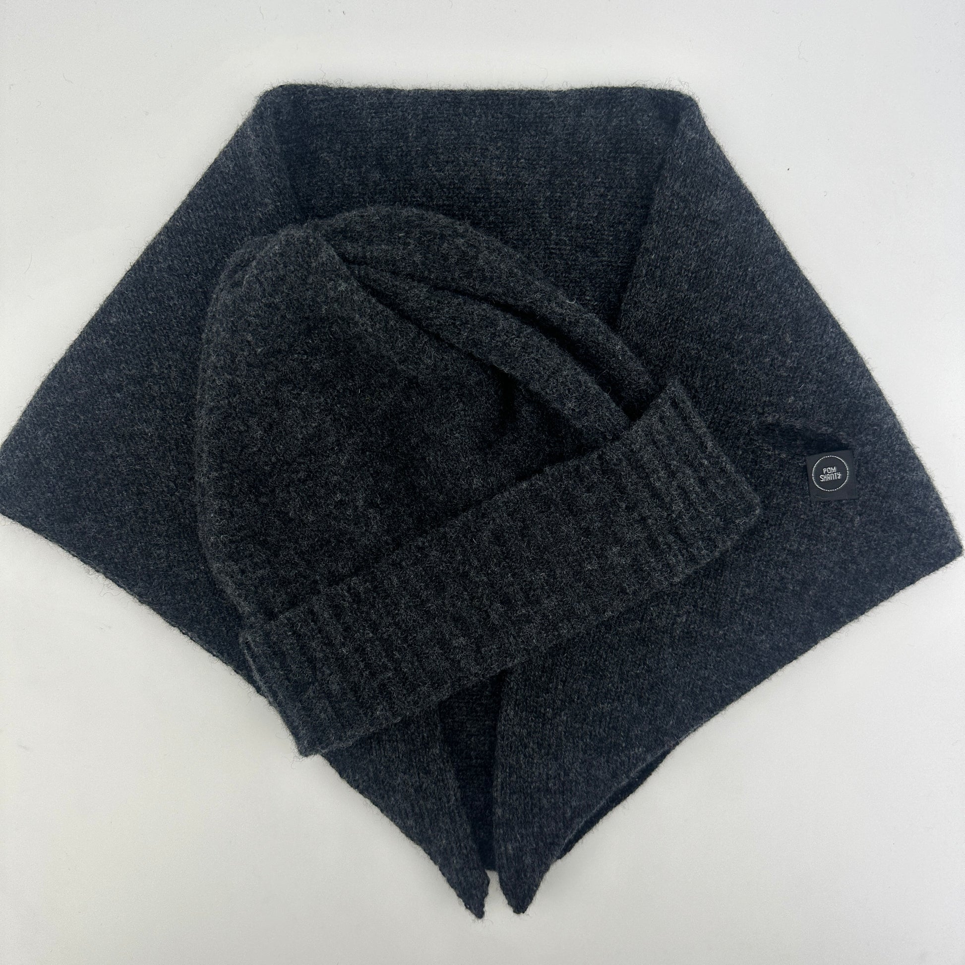 Charcoal grey coloured merino lambswool handcrafted knitted beanie with a double ribbed brim and kerchief lying flat on a white background