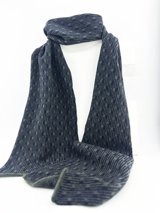 Olive Green and Navy Blue Metropolis geometric patterned handcrafted merino lambswool scarf hanging on a white display stand on a neutral background.  Pom Shanty Knitwear