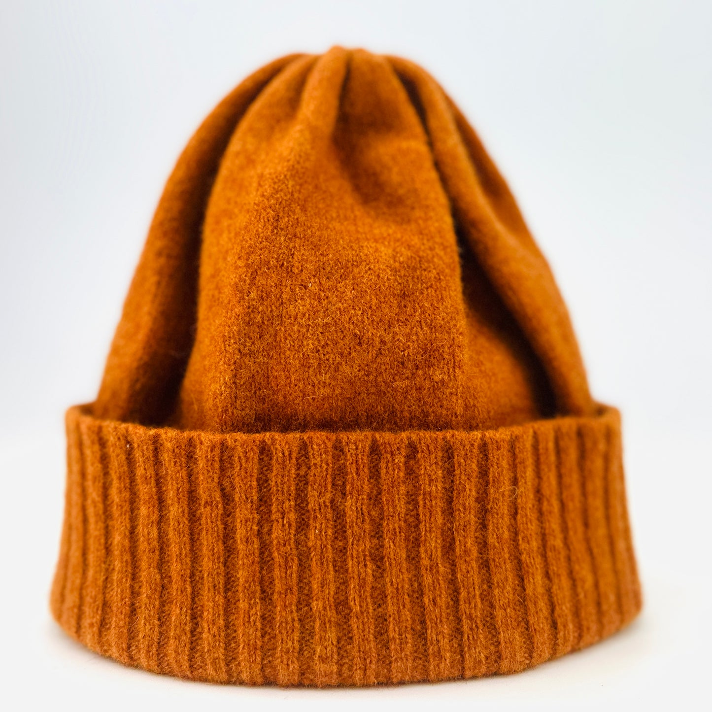 Rust coloured merino lambswool handcrafted knitted beanie propped up on white background