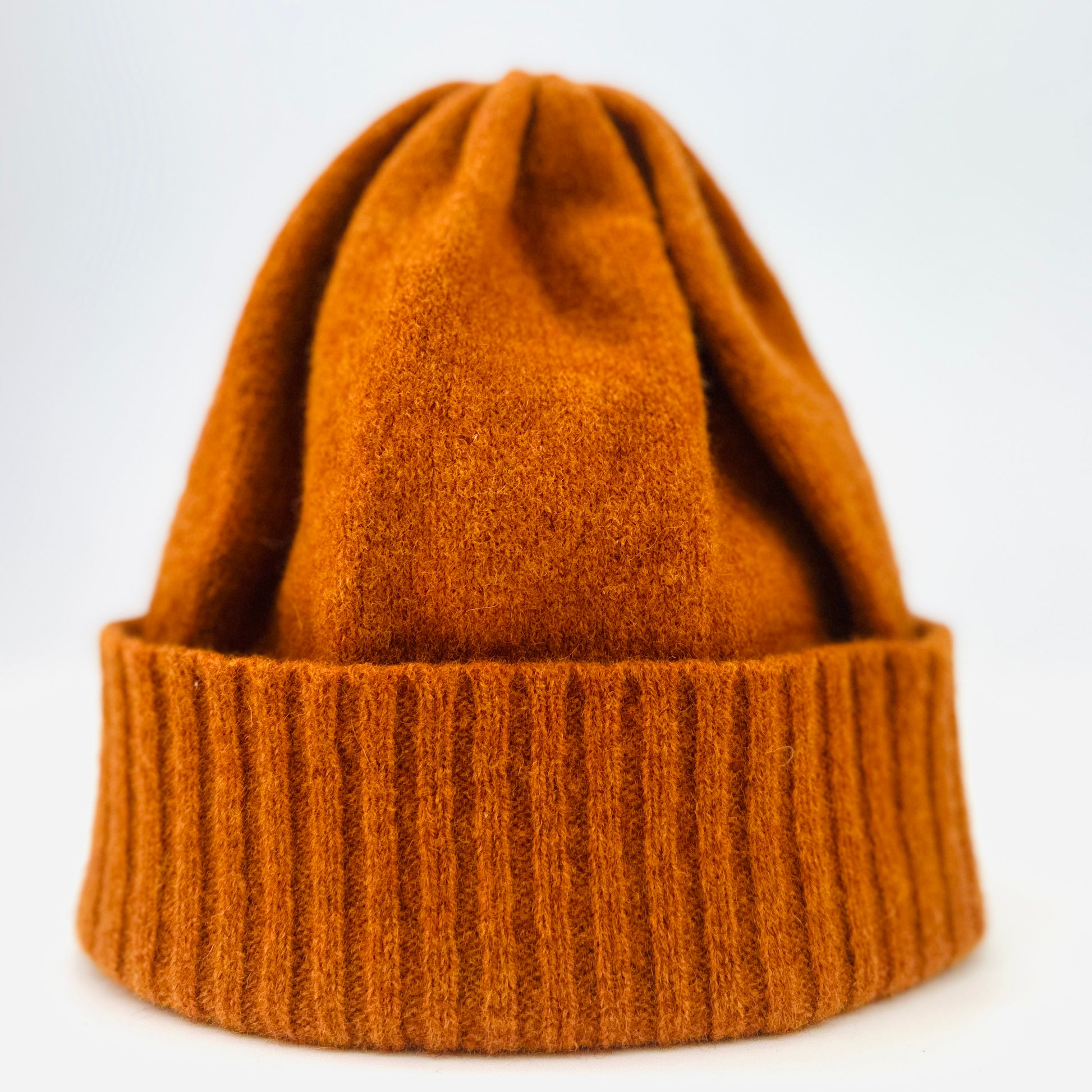 Rust coloured merino lambswool handcrafted knitted beanie propped up on white background