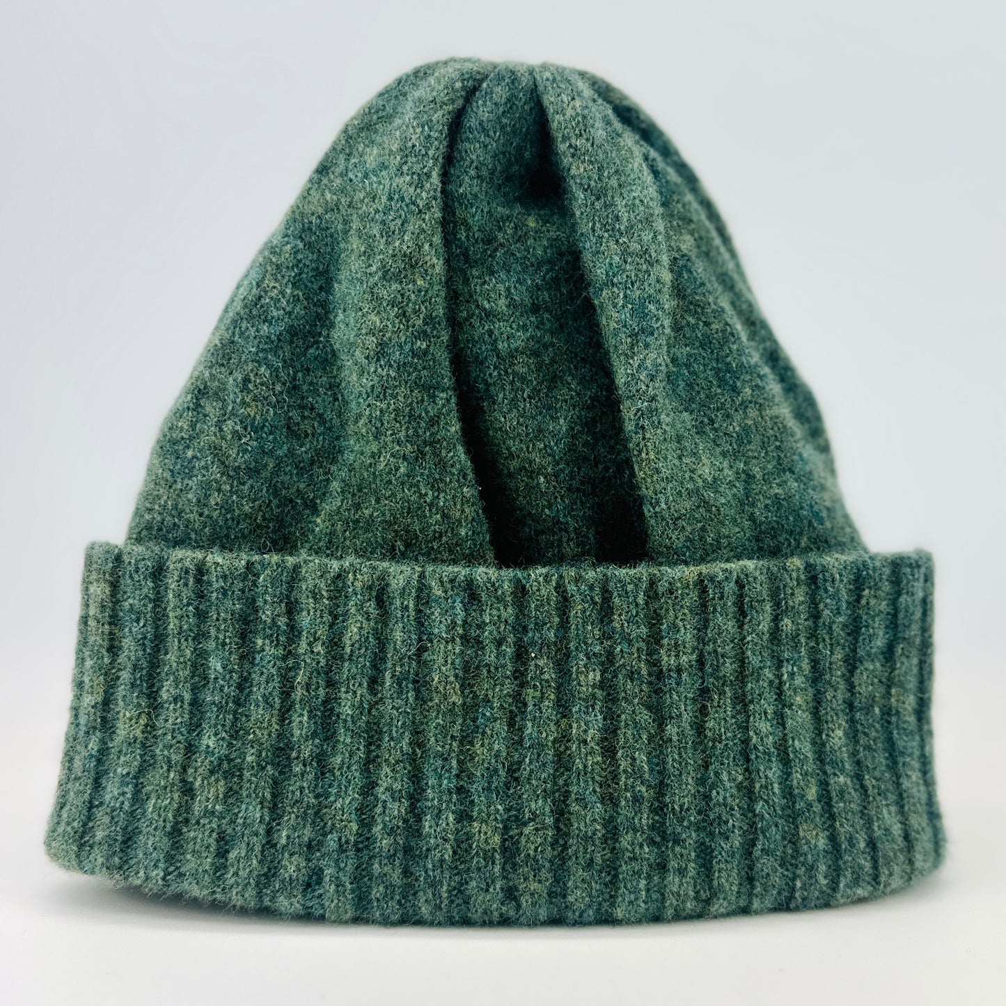 peacock green merino lambswool beanie with a double ribbed brim on a plain background.