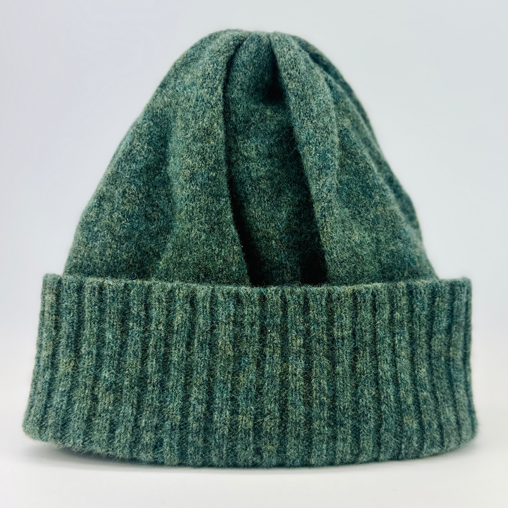 peacock green merino lambswool beanie with a double ribbed brim on a plain background.
