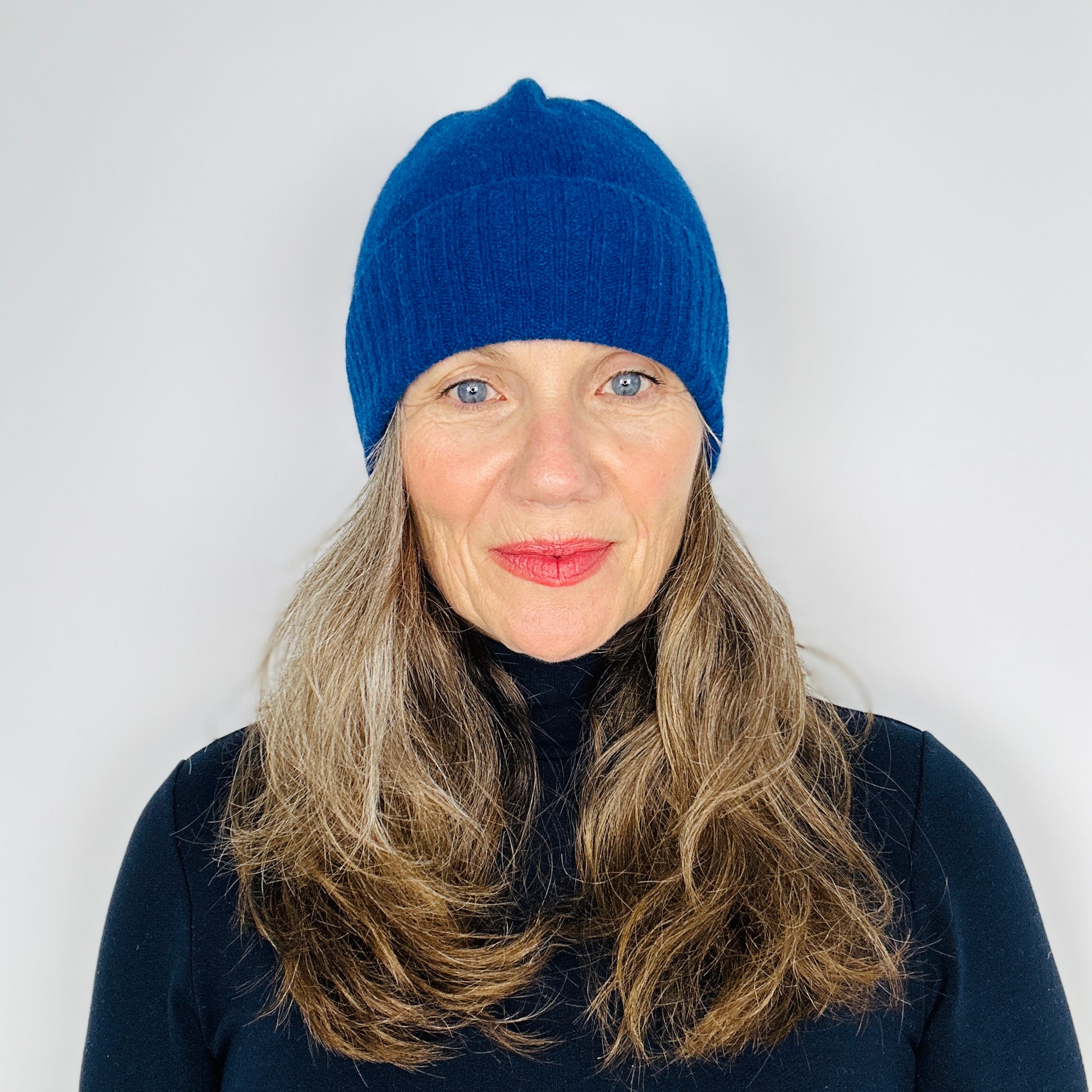 beautiful sexy woman in a black top wearing a dark blue merino lambswool beanie with a double ribbed brim on a plain background.