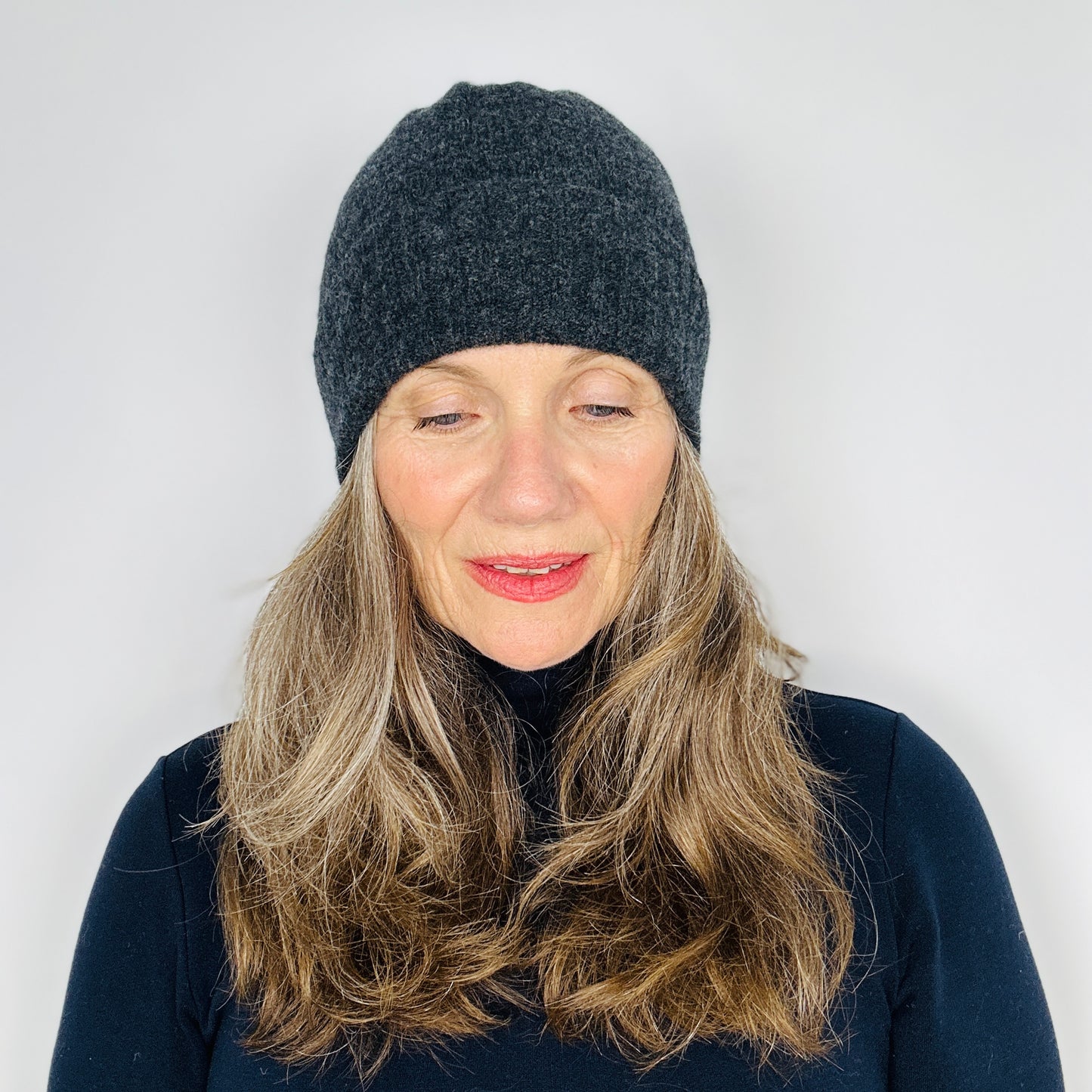 beautiful sexy woman in a black top wearing a charcoal grey merino lambswool beanie with a double ribbed brim on a plain background.