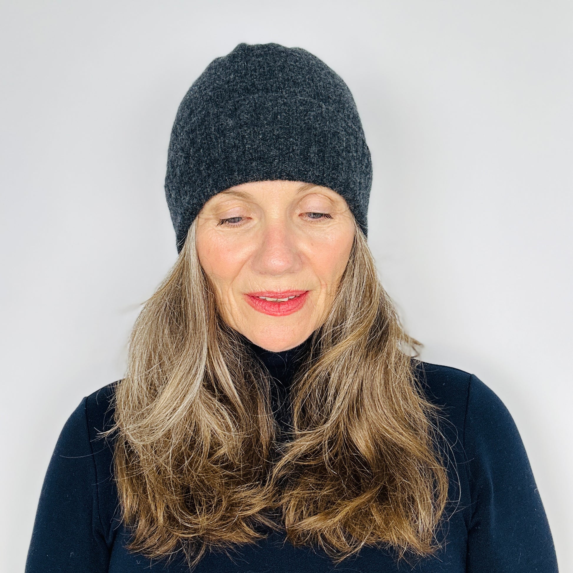 beautiful sexy woman in a black top wearing a charcoal grey merino lambswool beanie with a double ribbed brim on a plain background.