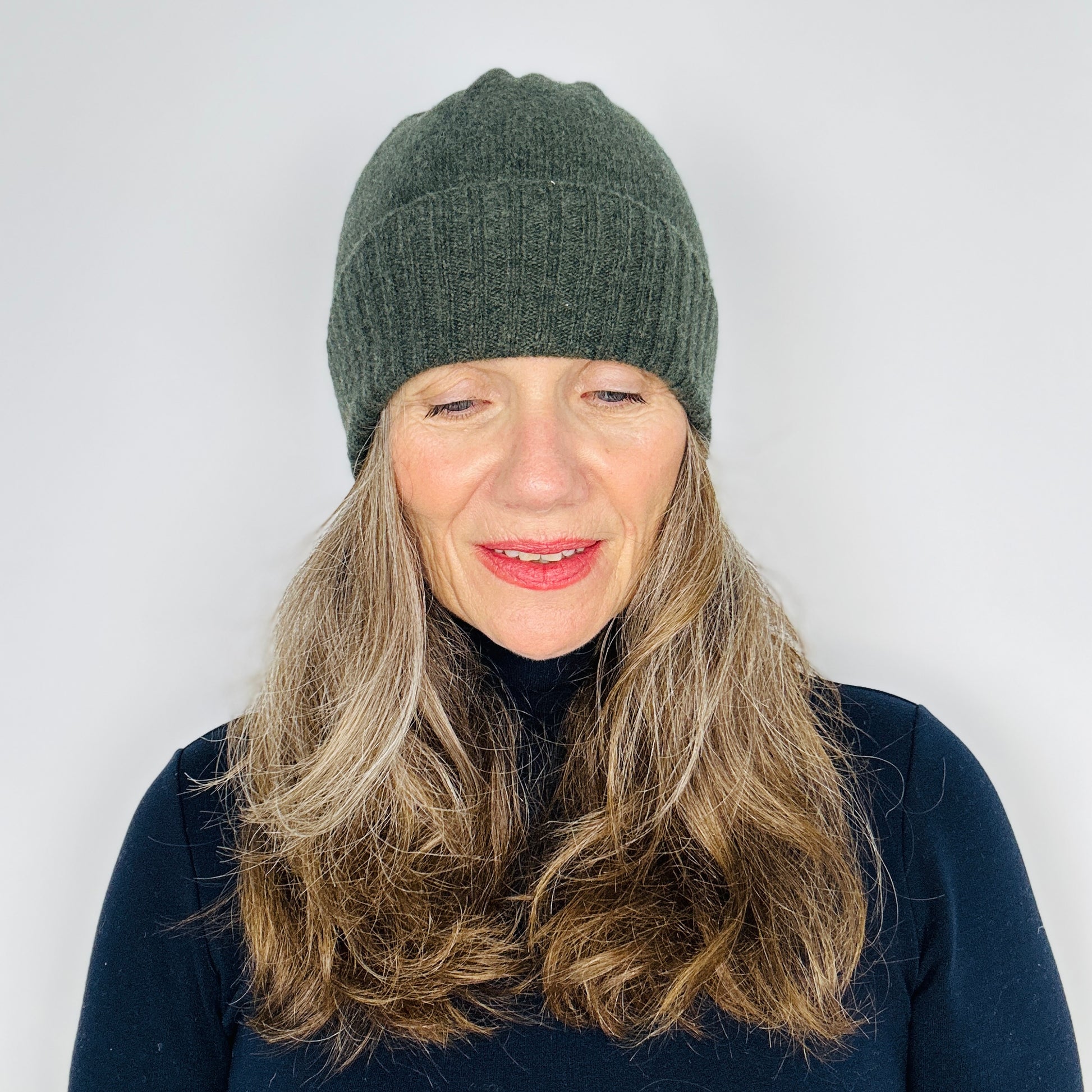 beautiful sexy woman in a black top wearing a olive green merino lambswool beanie with a double ribbed brim on a plain background.