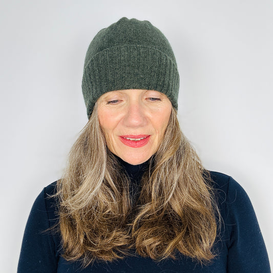beautiful sexy woman in a black top wearing a olive green merino lambswool beanie with a double ribbed brim on a plain background.