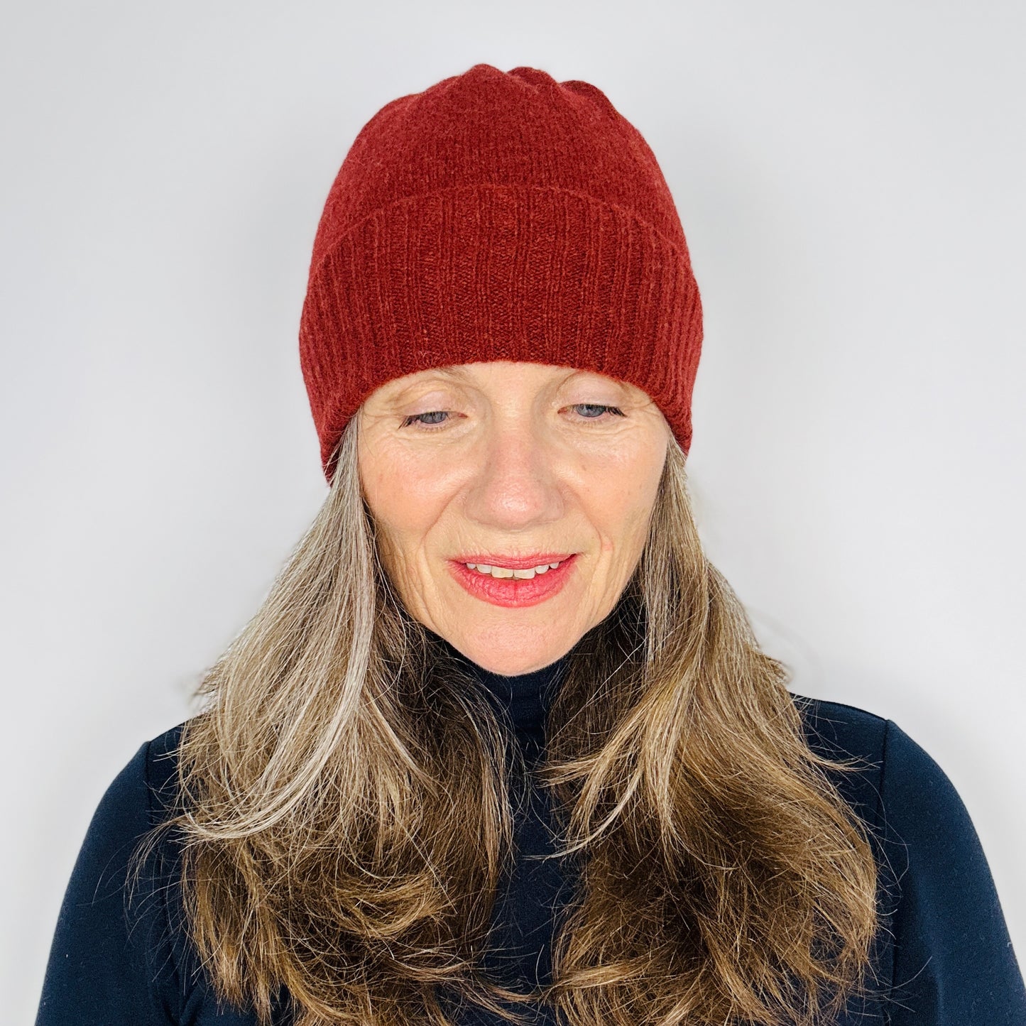 beautiful sexy woman in a black top wearing a sienna brown merino lambswool beanie with a double ribbed brim on a plain background.