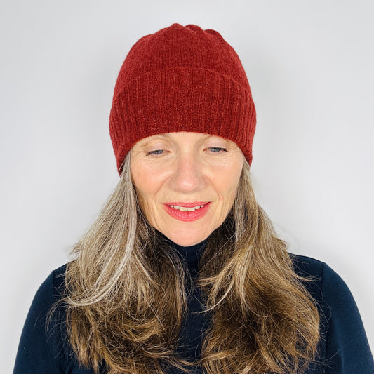 beautiful sexy woman in a black top wearing a sienna brown merino lambswool beanie with a double ribbed brim on a plain background.