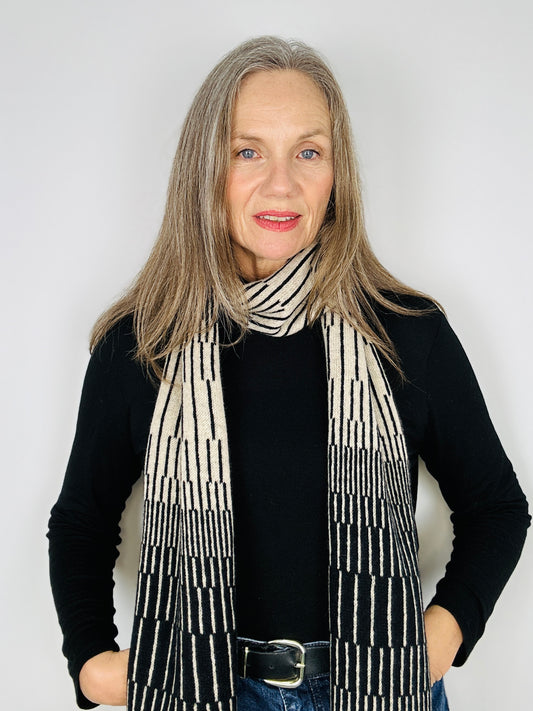 beautiful sexy woman in a black top wearing Black and Oatmeal handcrafted merino Lambswool striped Reverb Scarf against a neutral background.