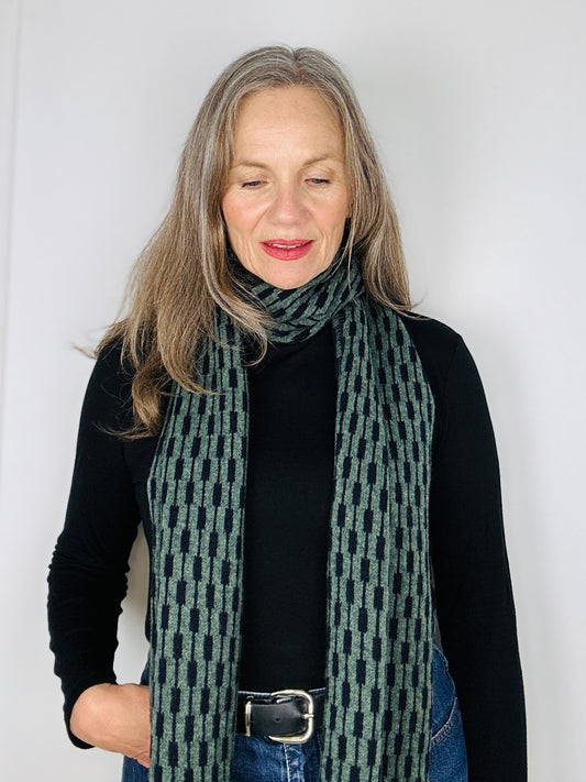 beautiful sexy woman in a black top wearing a peacock green and naby blue merino lambswool geometric patterned scarf on a plain background.