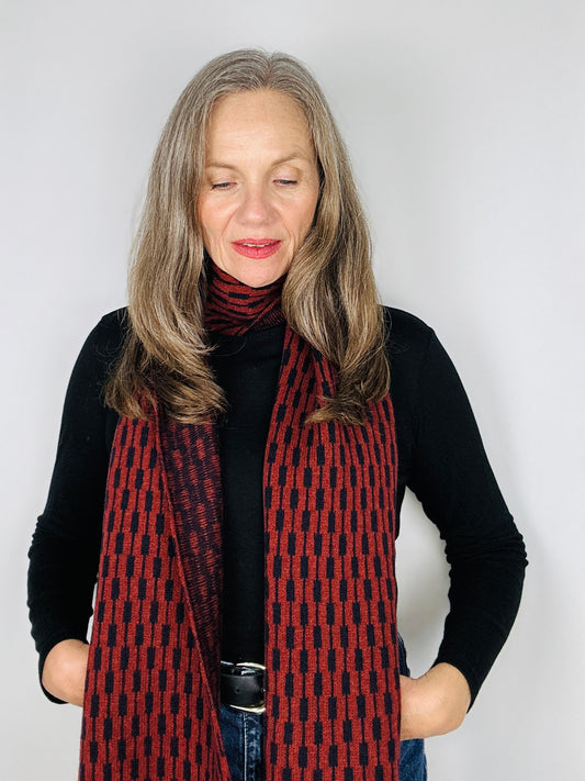 beautiful sexy woman in a black top wearing a sienna brown and navy blue merino lambswool geometric patterned scarf on a plain background.