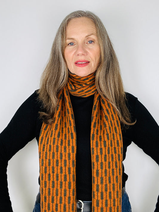 beautiful sexy woman in a black top wearing a rust and olive green merino lambswool geometric patterned scarf on a plain background.