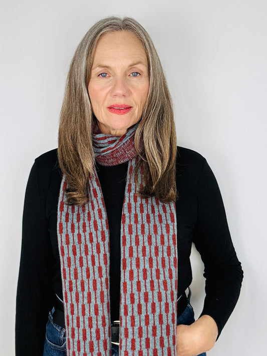 beautiful sexy woman in a black top wearing a sienna brown and caspian blue merino lambswool geometric patterned scarf on a plain background.