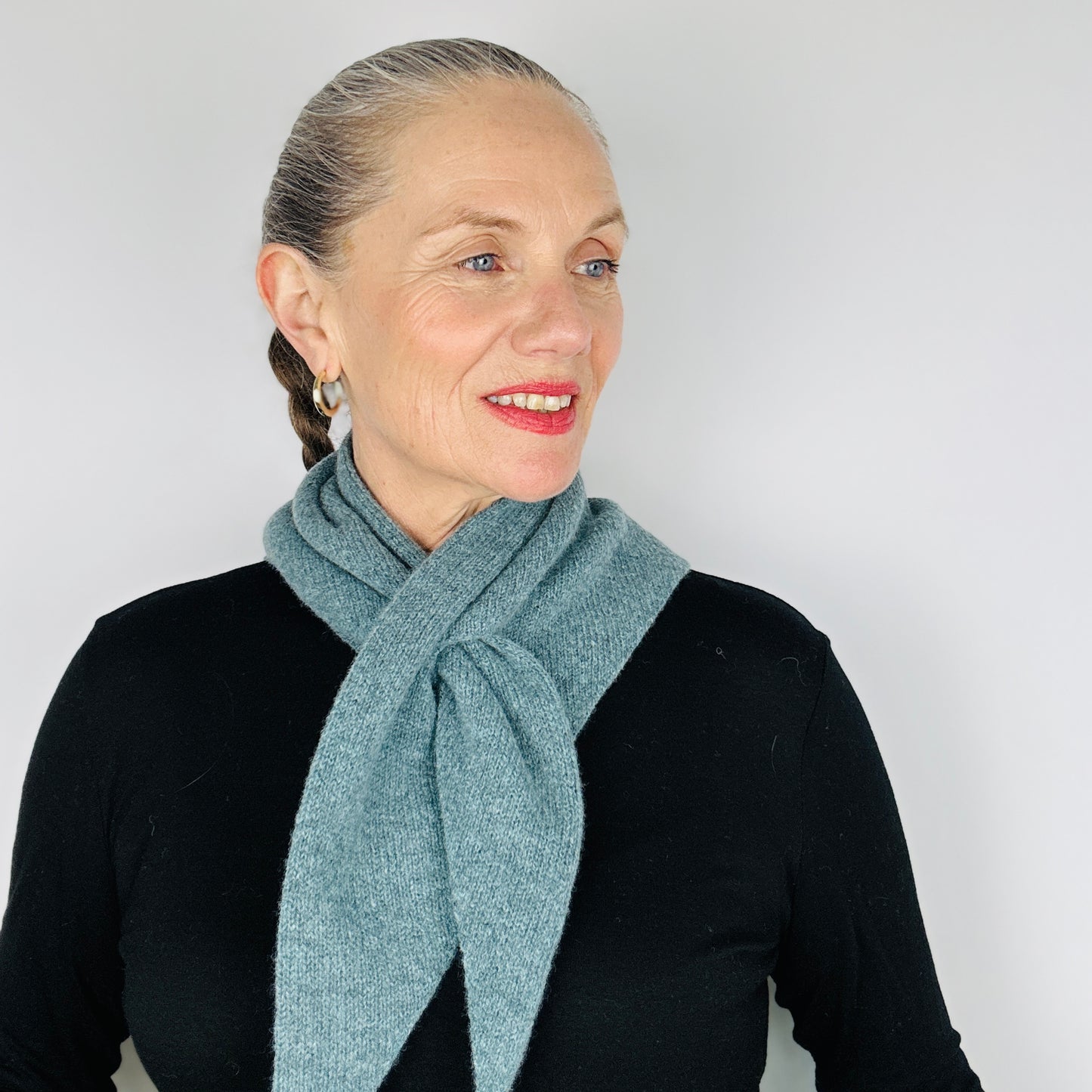 Beautiful sexy woman in a black top wearing merino lambswool double layer solid colour, caspian blue pull through triangle scarf / kerchief / neckerchief for women, men, unisex on a white backdrop