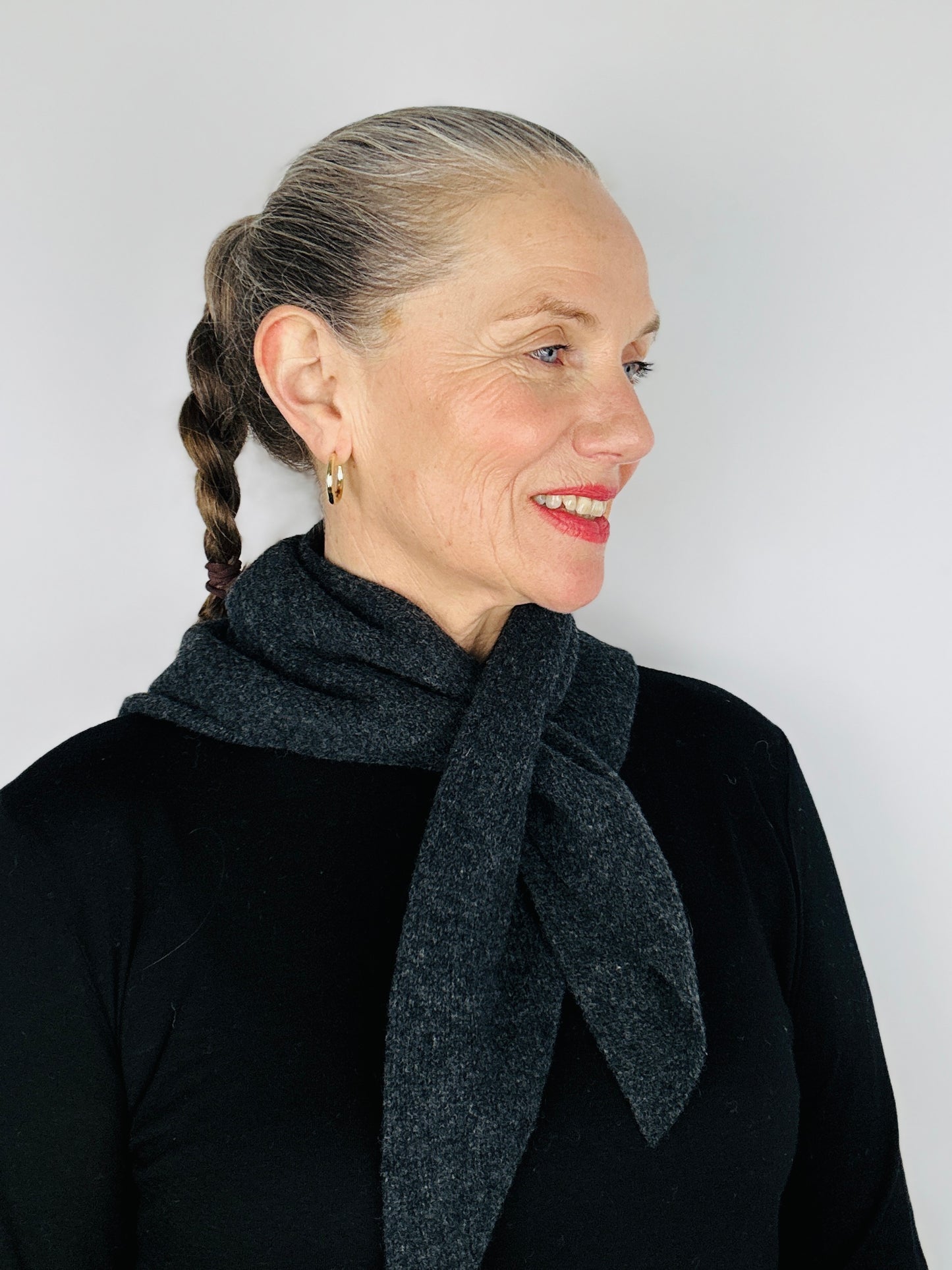 Beautiful sexy woman in a black top with her hair tied back and red lipstick on wearing merino lambswool double layer solid colour, charcoal grey pull through triangle scarf / kerchief / neckerchief for women, men, unisex on a neutral background