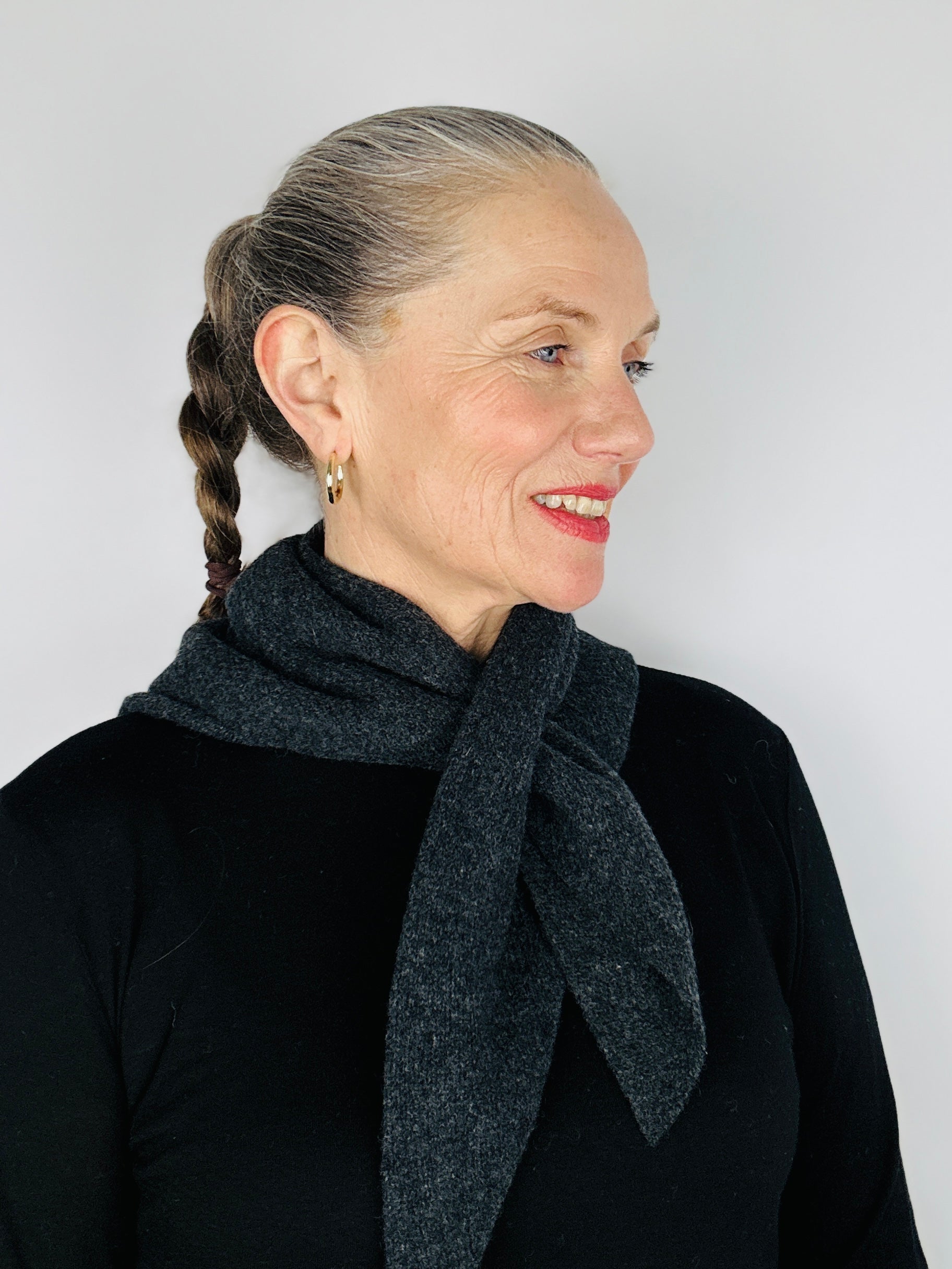 Beautiful sexy woman in a black top with her hair tied back and red lipstick on wearing merino lambswool double layer solid colour, charcoal grey pull through triangle scarf / kerchief / neckerchief for women, men, unisex on a neutral background