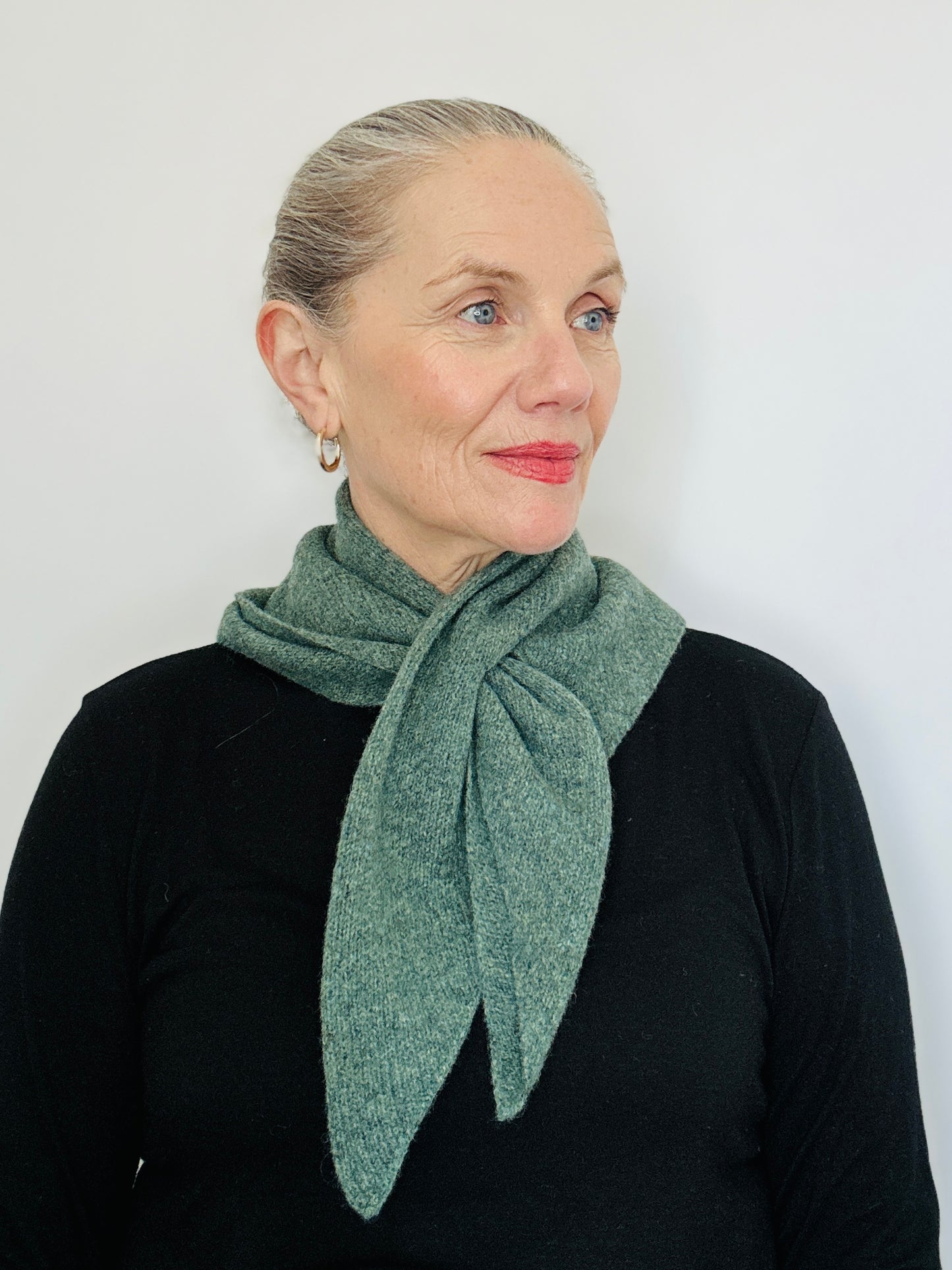 Beautiful sexy woman in a black top, with lipstick on and her hair tied back wearing merino lambswool double layer solid colour, peacock green pull through triangle scarf / kerchief / neckerchief for women, men, unisex in a black top.